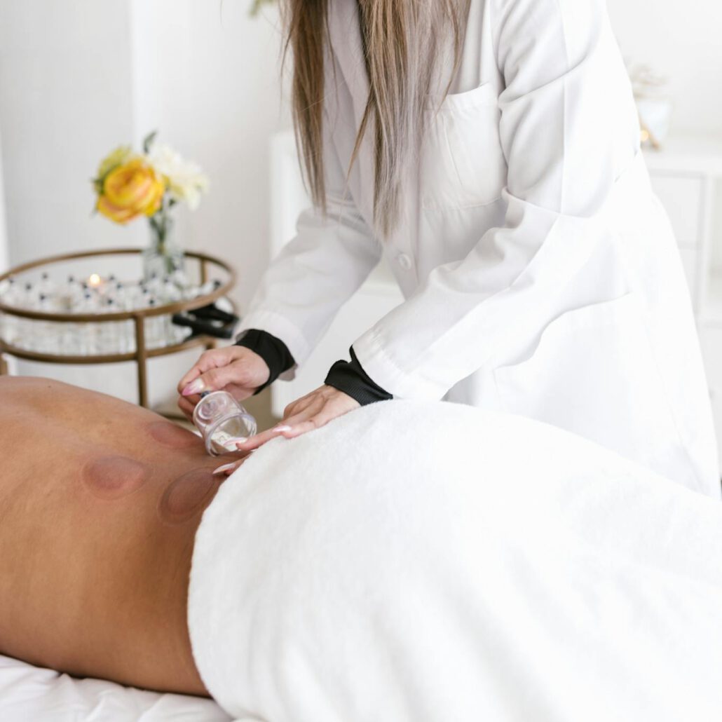 Female therapist applying cupping therapy to male patient in serene white setting.